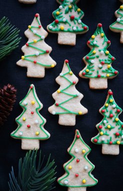 Koyu arkaplanda yeşil krema olan Noel ağacı şeklinde kurabiyeler.