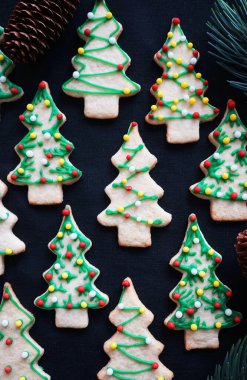 Koyu arkaplanda yeşil krema olan Noel ağacı şeklinde kurabiyeler.