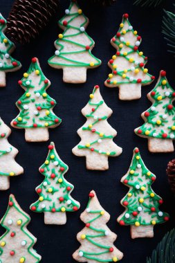Koyu arkaplanda yeşil krema olan Noel ağacı şeklinde kurabiyeler.