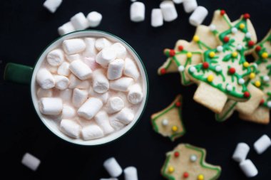 Siyah arka planda Noel ağacı şeklinde kurabiyelerin yanında marşmelov olan kakao.