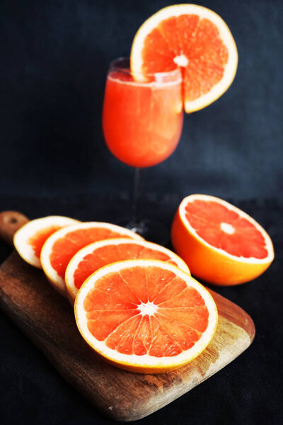 Grapefruit juice in a glass next to sliced grapefruit on a dark background