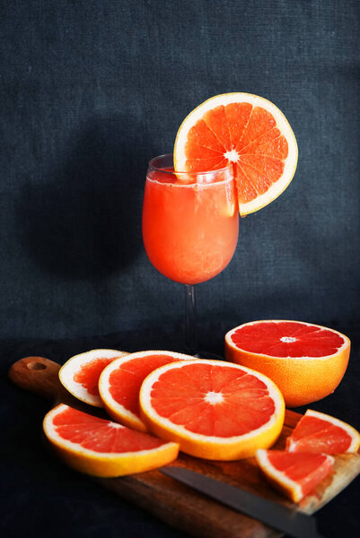 Grapefruit juice in a glass next to sliced grapefruit on a dark background