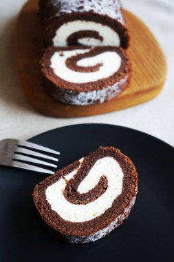 Tahtada vanilya kremalı çikolatalı dürüm, arka planda açık bir tabakta kesilmiş ruloların yanında.