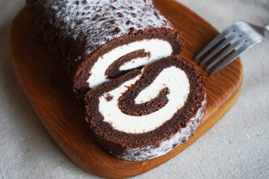 Çikolatalı sünger rulo, üzerinde vanilyalı krema ve tahta tahta tahta bir arka plan.