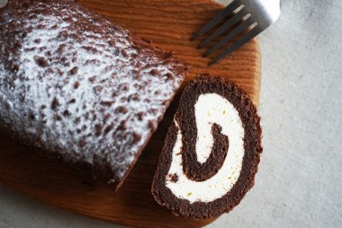 Çikolatalı sünger rulo, üzerinde vanilyalı krema ve tahta tahta tahta bir arka plan.