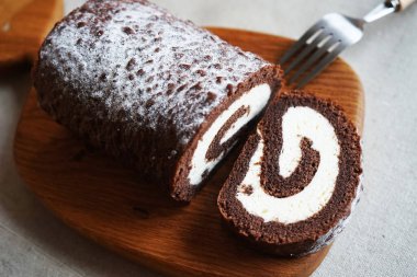 Çikolatalı sünger rulo, üzerinde vanilyalı krema ve tahta tahta tahta bir arka plan.