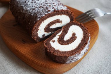 Çikolatalı sünger rulo, üzerinde vanilyalı krema ve tahta tahta tahta bir arka plan.