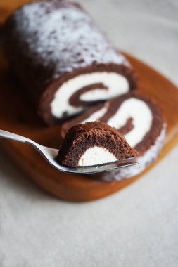 Çikolatalı sünger rulo, üzerinde vanilyalı krema ve tahta tahta tahta bir arka plan.