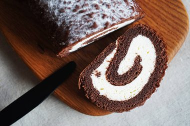 Çikolatalı sünger rulo, üzerinde vanilyalı krema ve tahta tahta tahta bir arka plan.