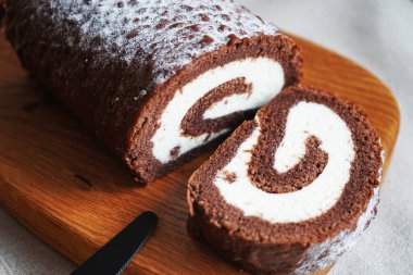 Çikolatalı sünger rulo, üzerinde vanilyalı krema ve tahta tahta tahta bir arka plan.