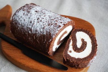 Çikolatalı sünger rulo, üzerinde vanilyalı krema ve tahta tahta tahta bir arka plan.