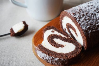 Çikolatalı sünger rulo vanilya kremalı tahta tahtada bir fincan çayın yanında.