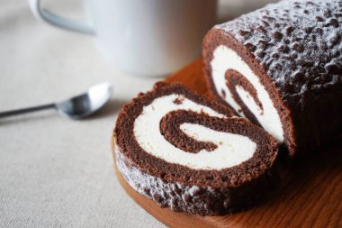 Çikolatalı sünger rulo vanilya kremalı tahta tahtada bir fincan çayın yanında.