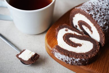 Çikolatalı sünger rulo vanilya kremalı tahta tahtada bir fincan çayın yanında.