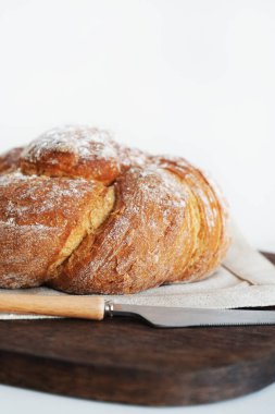 Tahtada taze ekmek ve beyaz arka planda bir bıçağın yanında keten masa örtüsü.