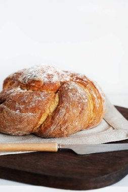 Tahtada taze ekmek ve beyaz arka planda bir bıçağın yanında keten masa örtüsü.