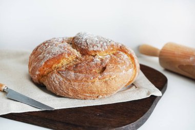 Tahtada taze ekmek ve beyaz arka planda bir bıçağın yanında keten masa örtüsü.