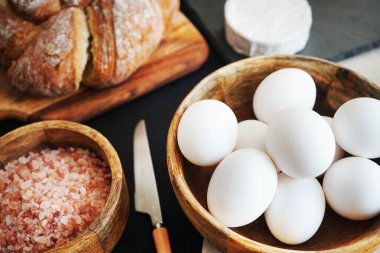 Tahta bir kasede beyaz tavuk yumurtası, ekmeğin yanında peynir ve kalın pembe tuz.