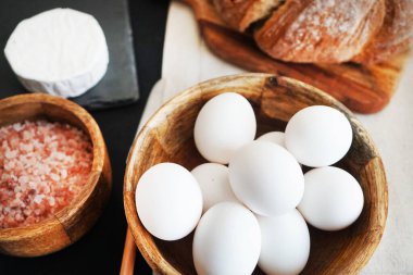 Tahta bir kasede beyaz tavuk yumurtası, ekmeğin yanında peynir ve kalın pembe tuz.