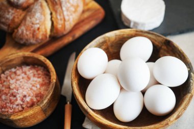 Tahta bir kasede beyaz tavuk yumurtası, ekmeğin yanında peynir ve kalın pembe tuz.