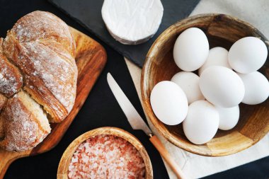 Tahta bir kasede beyaz tavuk yumurtası, ekmeğin yanında peynir ve kalın pembe tuz.