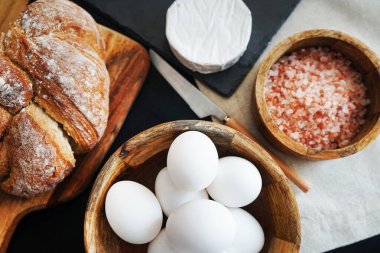 Tahta bir kasede beyaz tavuk yumurtası, ekmeğin yanında peynir ve kalın pembe tuz.