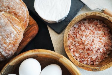 Tahta bir kasede beyaz tavuk yumurtası, ekmeğin yanında peynir ve kalın pembe tuz.