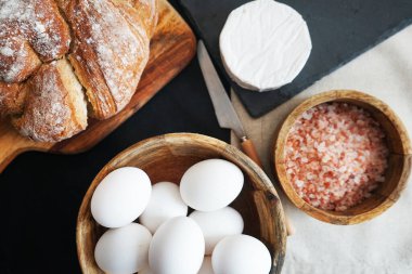 Tahta bir kasede beyaz tavuk yumurtası, ekmeğin yanında peynir ve kalın pembe tuz.