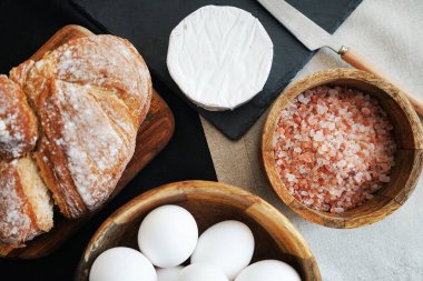 Tahta bir kasede beyaz tavuk yumurtası, ekmeğin yanında peynir ve kalın pembe tuz.