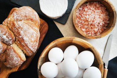 Tahta bir kasede beyaz tavuk yumurtası, ekmeğin yanında peynir ve kalın pembe tuz.