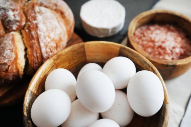 Tahta bir kasede beyaz tavuk yumurtası, ekmeğin yanında peynir ve kalın pembe tuz.