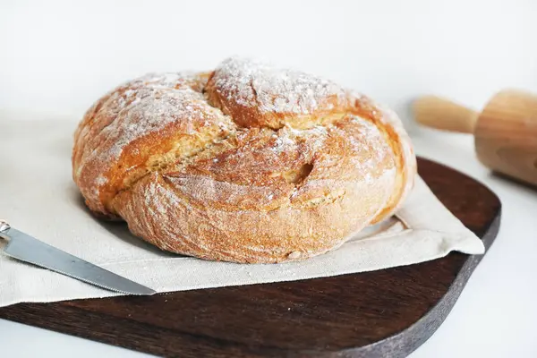 Tahtada taze ekmek ve beyaz arka planda bir bıçağın yanında keten masa örtüsü.