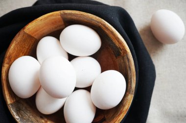 Beyaz tavuk yumurtaları, beyaz arka planda, siyah havluyla ahşap bir kasede.