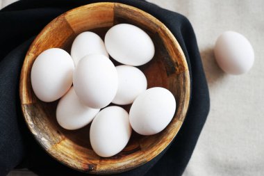 Beyaz tavuk yumurtaları, beyaz arka planda, siyah havluyla ahşap bir kasede.