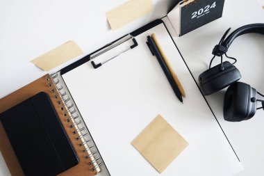 Not defterlerinin, takvimin, çıkartmaların, kalemlerin ve siyah kulaklıkların yanında kağıt olan klasör