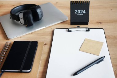 Klipsi, not defterleri, kalemleri, takvimi, dizüstü bilgisayarı ve kulaklığı olan işyeri