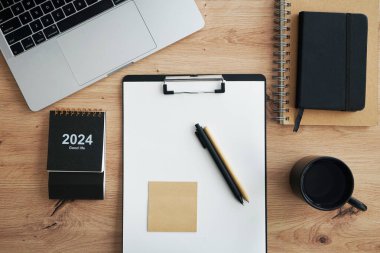 Açık dizüstü bilgisayarı, dizinleri, klasörleri, kalemi, gözlükleri, takvimi ve kahveli siyah kupası olan işyeri