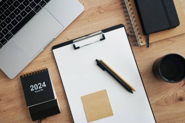 Açık dizüstü bilgisayarı, dizinleri, klasörleri, kalemi, gözlükleri, takvimi ve kahveli siyah kupası olan işyeri