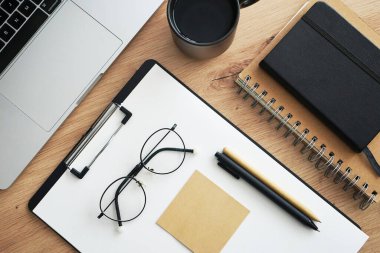 Açık dizüstü bilgisayarı, dizinleri, klasörleri, kalemi, gözlükleri, takvimi ve kahveli siyah kupası olan işyeri