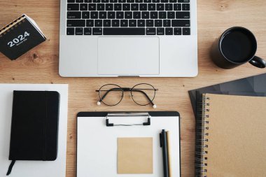 Açık dizüstü bilgisayarı, dizinleri, klasörleri, kalemi, gözlükleri, takvimi ve kahveli siyah kupası olan işyeri