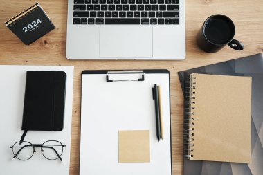 Açık dizüstü bilgisayarı, dizinleri, klasörleri, kalemi, gözlükleri, takvimi ve kahveli siyah kupası olan işyeri