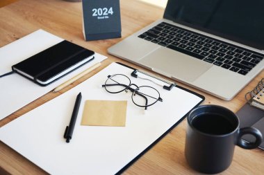 Açık dizüstü bilgisayarı, dizinleri, klasörleri, kalemi, gözlükleri, takvimi ve kahveli siyah kupası olan işyeri