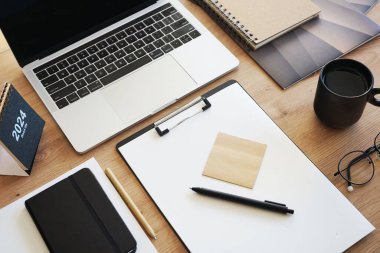Açık dizüstü bilgisayarı, dizinleri, klasörleri, kalemi, gözlükleri, takvimi ve kahveli siyah kupası olan işyeri