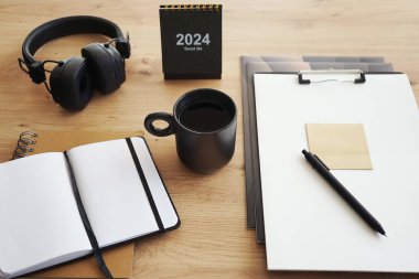 Not defterleri, klasörleri, kalemi, kulaklıkları, takvimi ve kahveli siyah kupası olan masaüstü