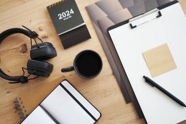 Not defterleri, klasörleri, kalemi, kulaklıkları, takvimi ve kahveli siyah kupası olan masaüstü