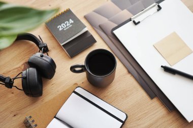 Not defterleri, klasörleri, kalemi, kulaklıkları, takvimi ve kahveli siyah kupası olan masaüstü