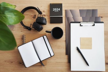 Not defterleri, klasörleri, kalemi, kulaklıkları, takvimi ve kahveli siyah kupası olan masaüstü