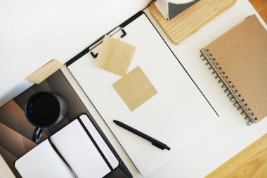 Not defterleri, klasörler, çıkartmalar, takvim, bardaklar, kalemler, masa lambası açık arkaplanda siyah bir fincan kahvenin yanında.