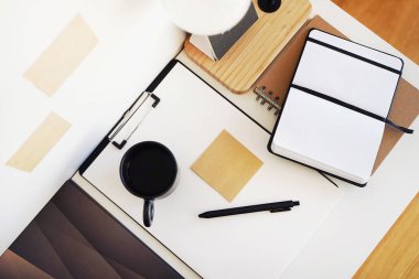 Not defterleri, klasörler, çıkartmalar, takvim, bardaklar, kalemler, masa lambası açık arkaplanda siyah bir fincan kahvenin yanında.