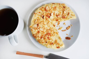 Beyaz bir tabakta bademli kek, beyaz arka planda bir fincan çayın yanında.